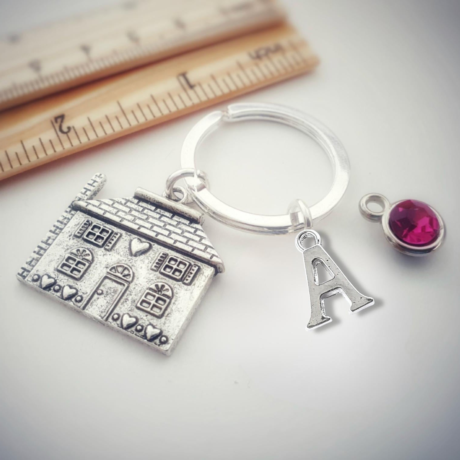 Keychain with house charm, letter 'A' charm, and pink gemstone on a light background