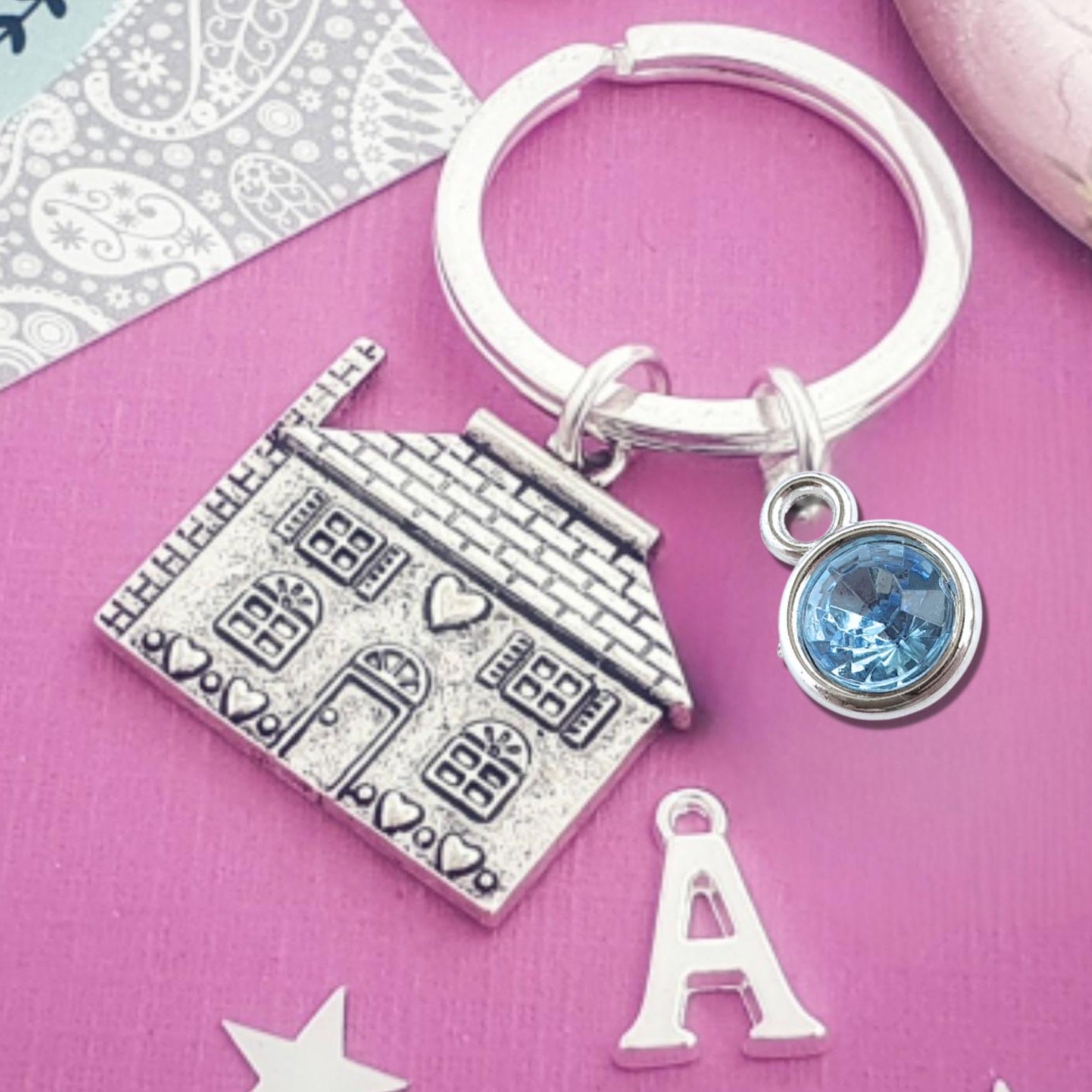 Keychain with house charm, blue gemstone, and letter 'A' on a pink background
