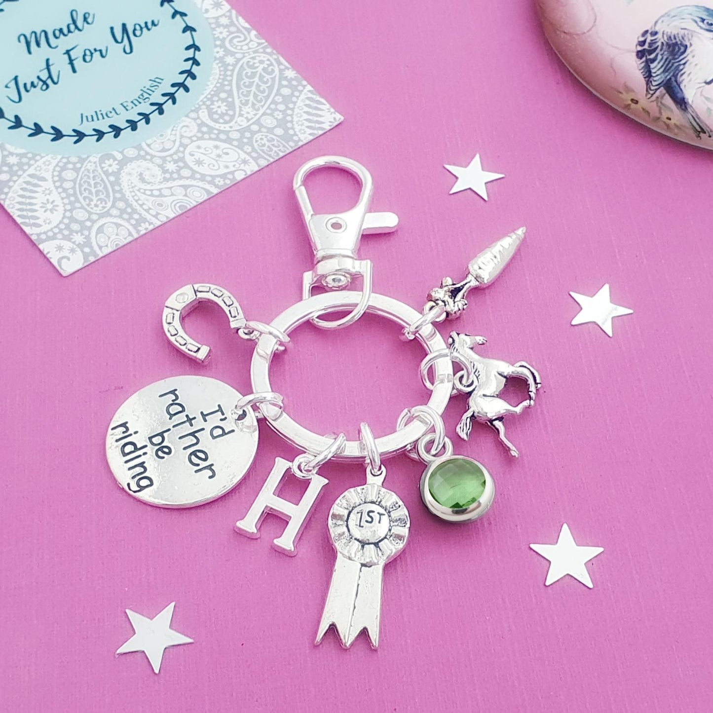 Silver charm keychain with various charms on a pink background