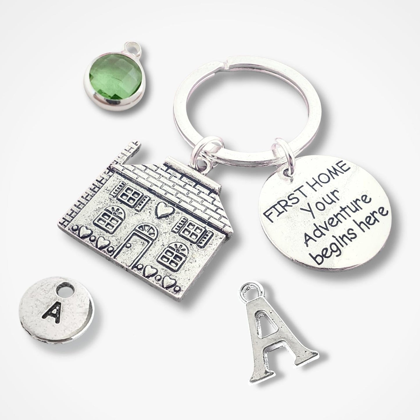 Silver keychain with house charm, green gemstone, and 'First Home Your Adventure Begins Here' tag on a white background