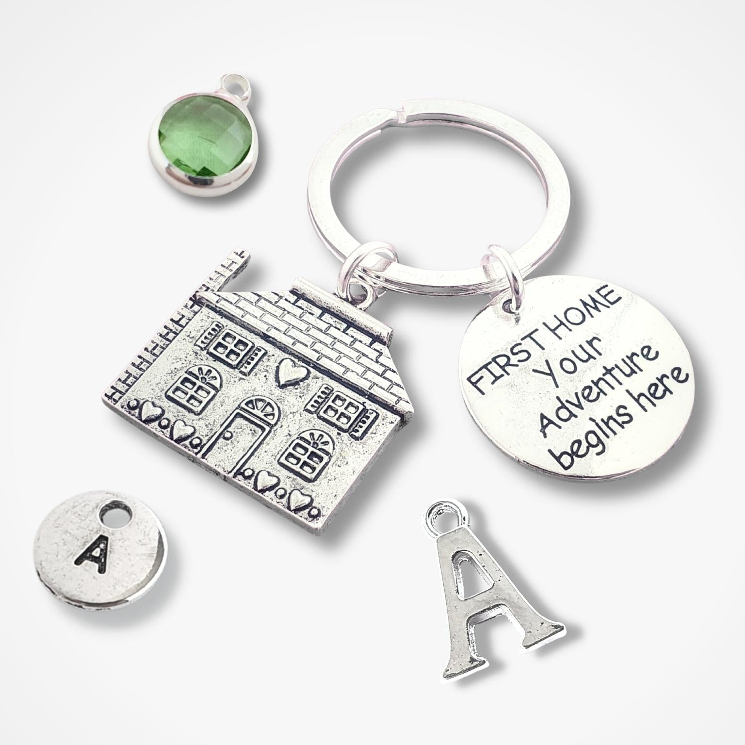 Silver keychain with house charm, green gemstone, and 'First Home Your Adventure Begins Here' tag on a white background