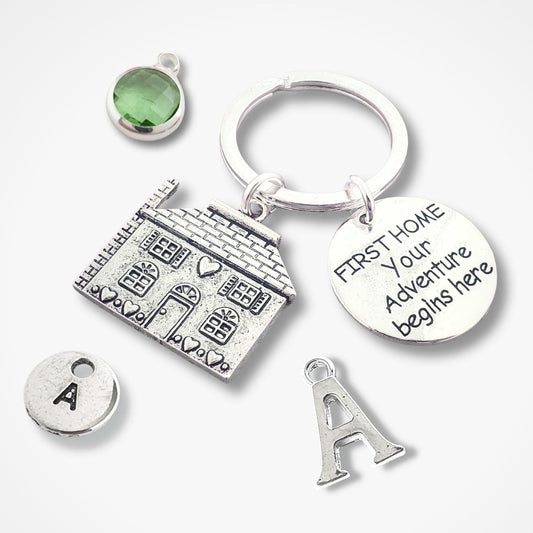 Silver keychain with house charm, green gemstone, and 'First Home Your Adventure Begins Here' tag on a white background