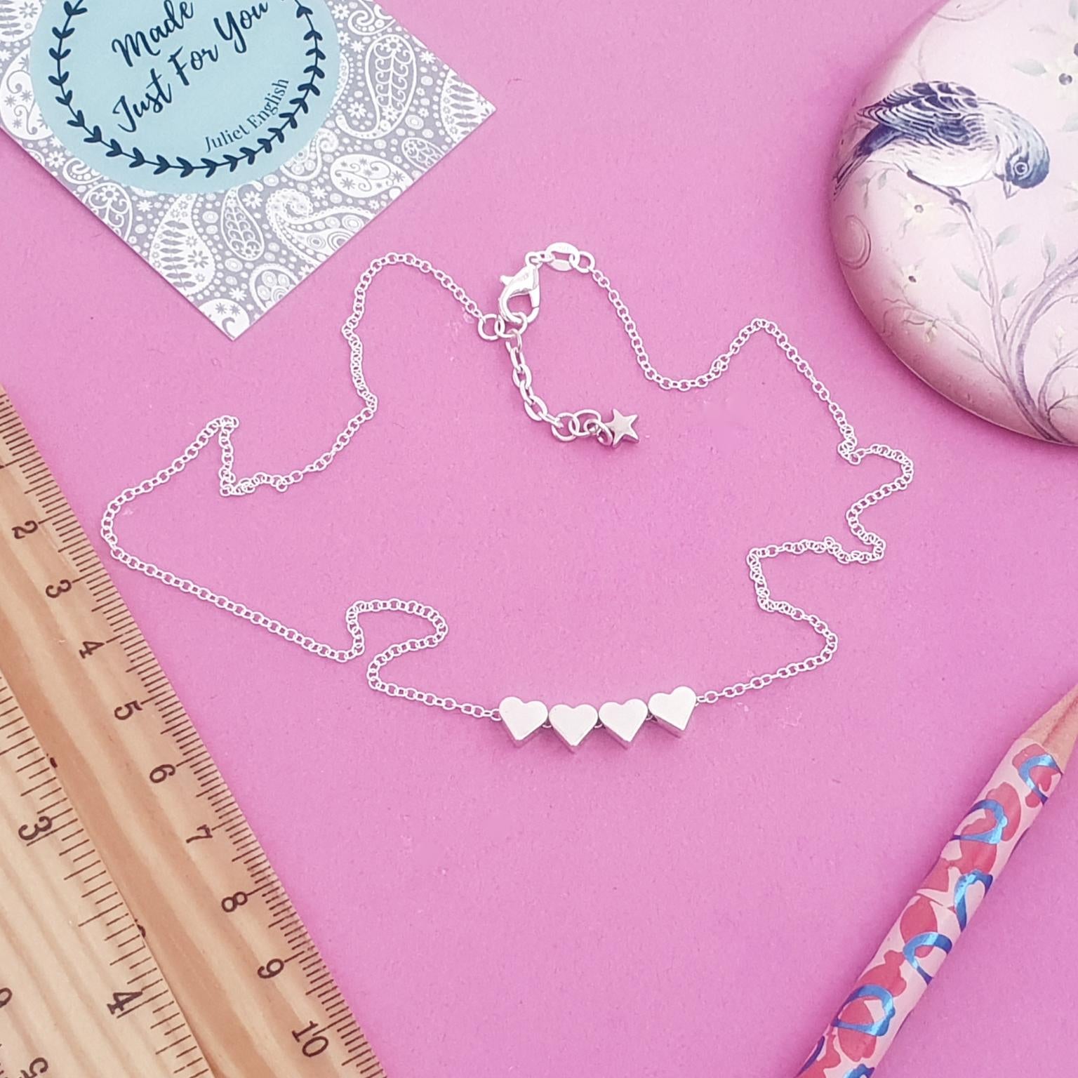 Silver necklace with heart pendants on a pink background with a ruler and pencil.