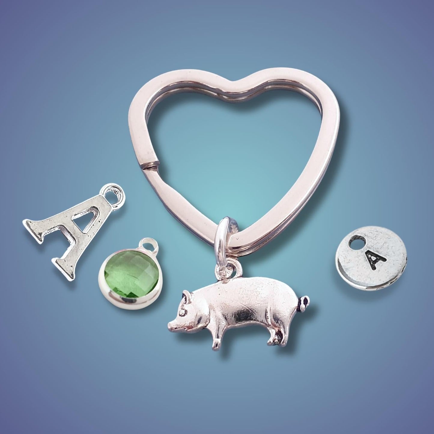 Collection of silver charms including a heart, letter 'A', pig, and green gemstone on a gradient blue background.