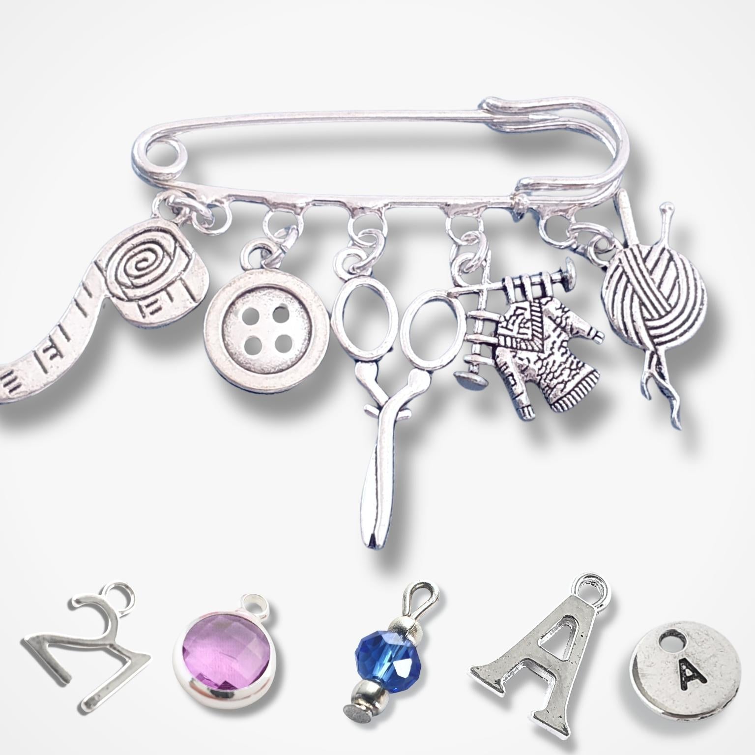 Silver brooch with various knitting themed charms on a white background