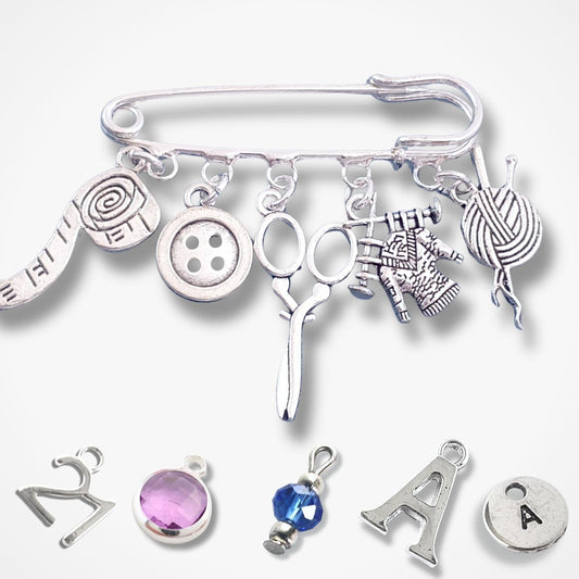 Silver brooch with various knitting themed charms on a white background