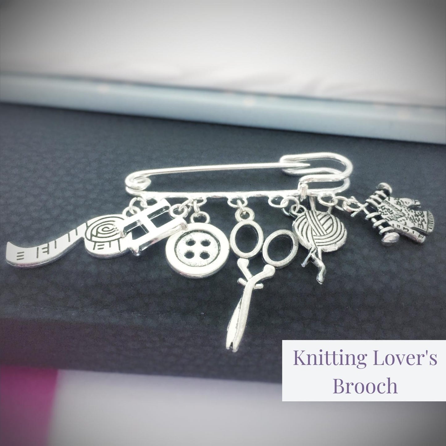 Silver brooch with knitting-themed charms on a dark fabric background
