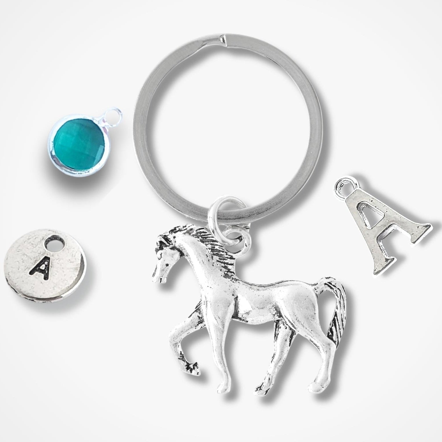 Silver keychain with horse charm, round turquoise charm, and circular charm with letter 'A' on a white background