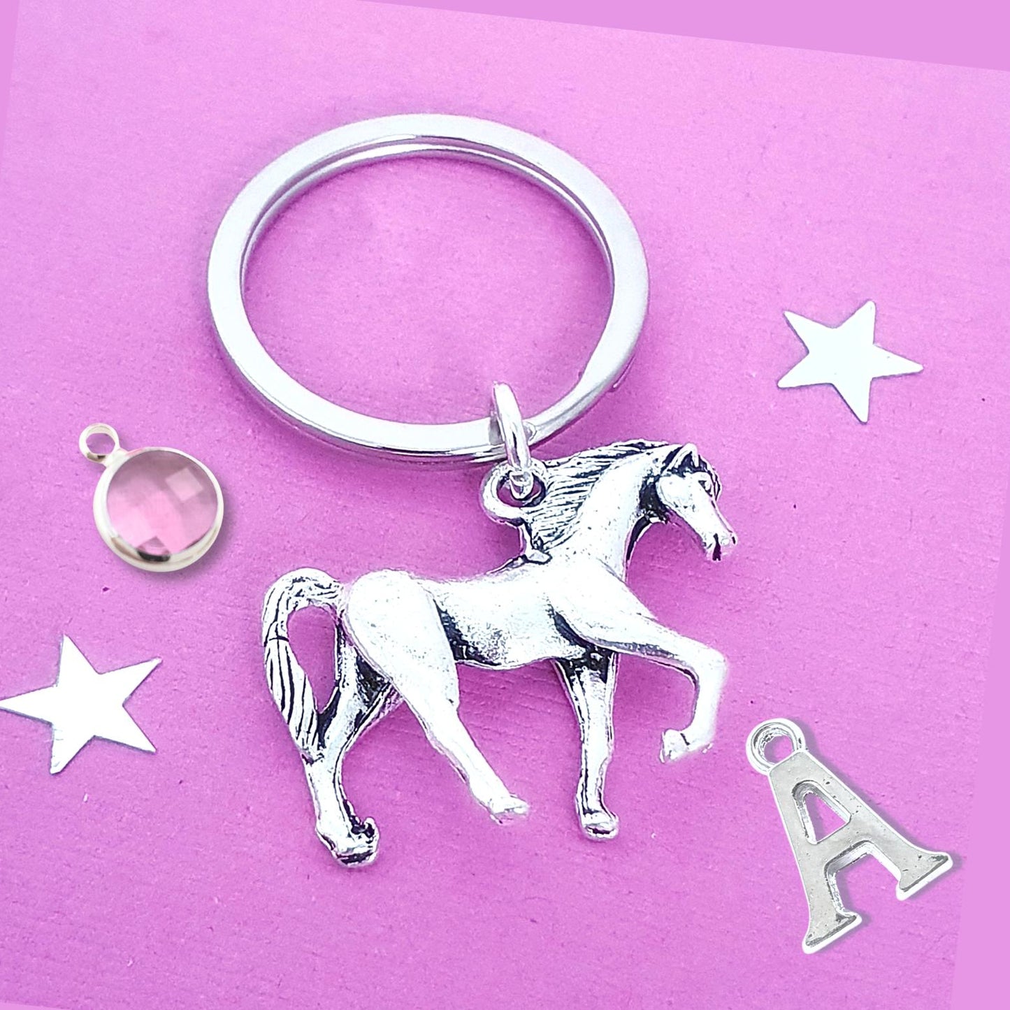 Silver horse keychain with additional charms on a pink background