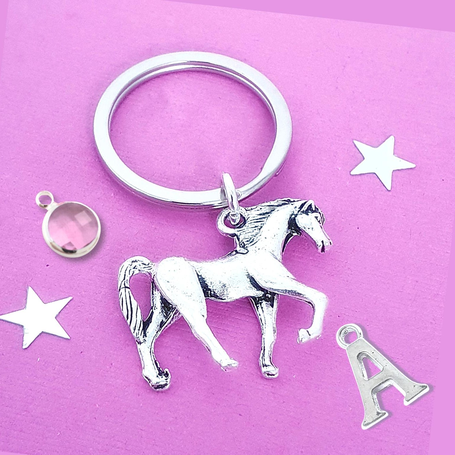 Silver horse keychain with additional charms on a pink background