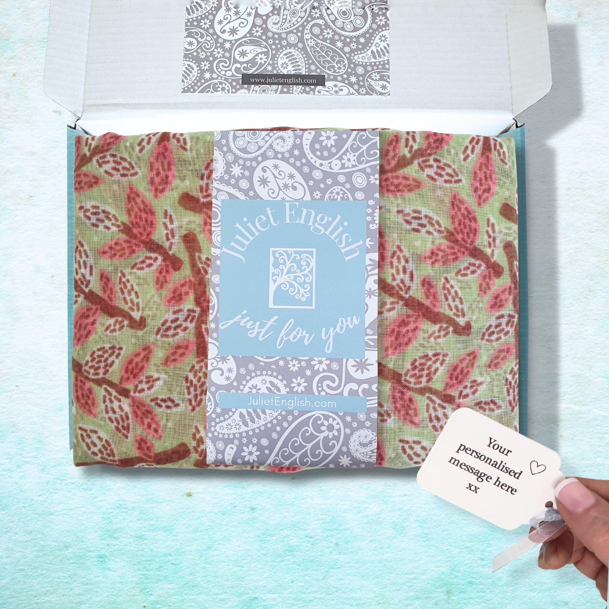 Packaged scarf with floral patterns and a personalized card on a light blue background