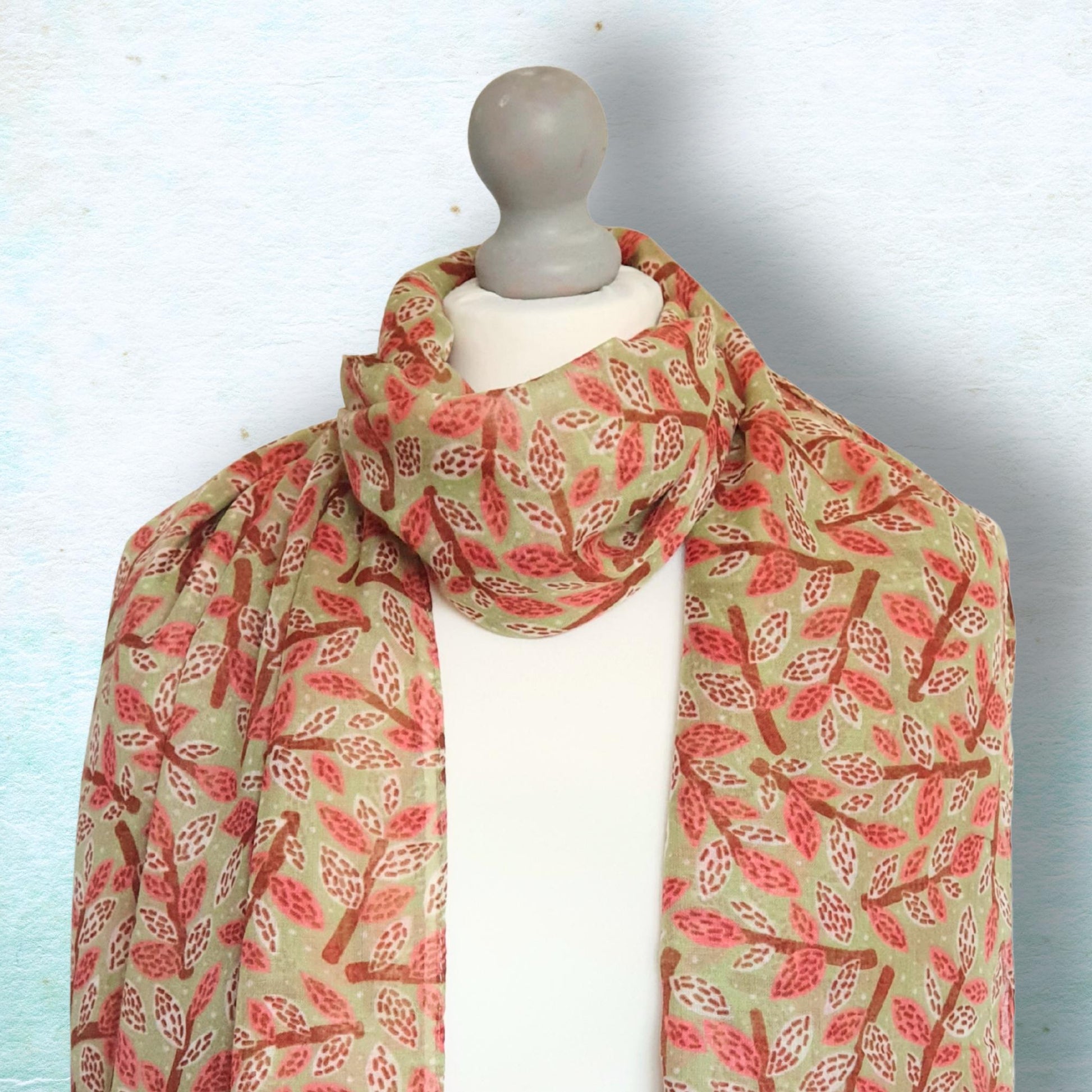 Mannequin wearing a dusky rose, brown and green leaf and branch patterned scarf against a light blue background