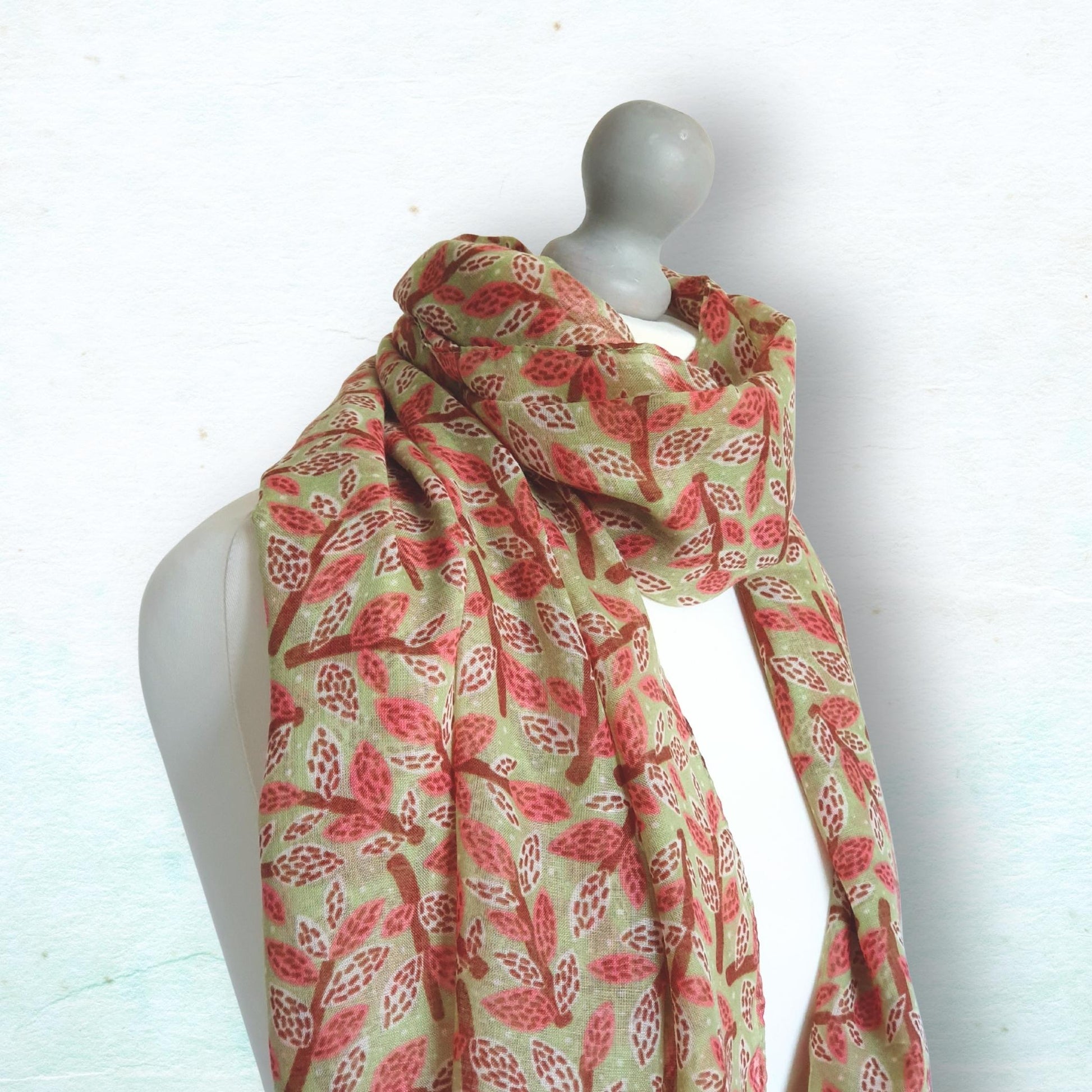 Mannequin wearing a dusty rose, brown and green leaf and branch patterned scarf on a white background