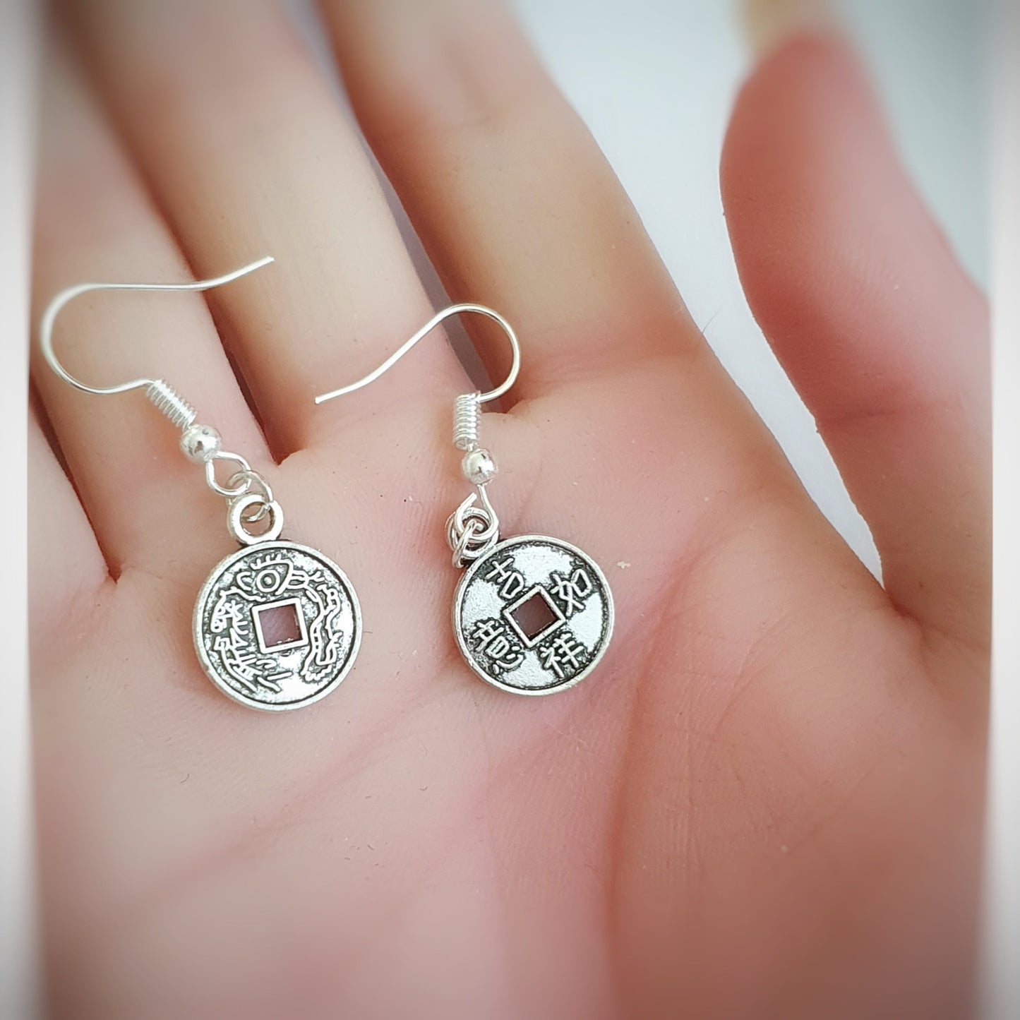 Silver lucky coin earrings with circular designs held between fingers on a light background