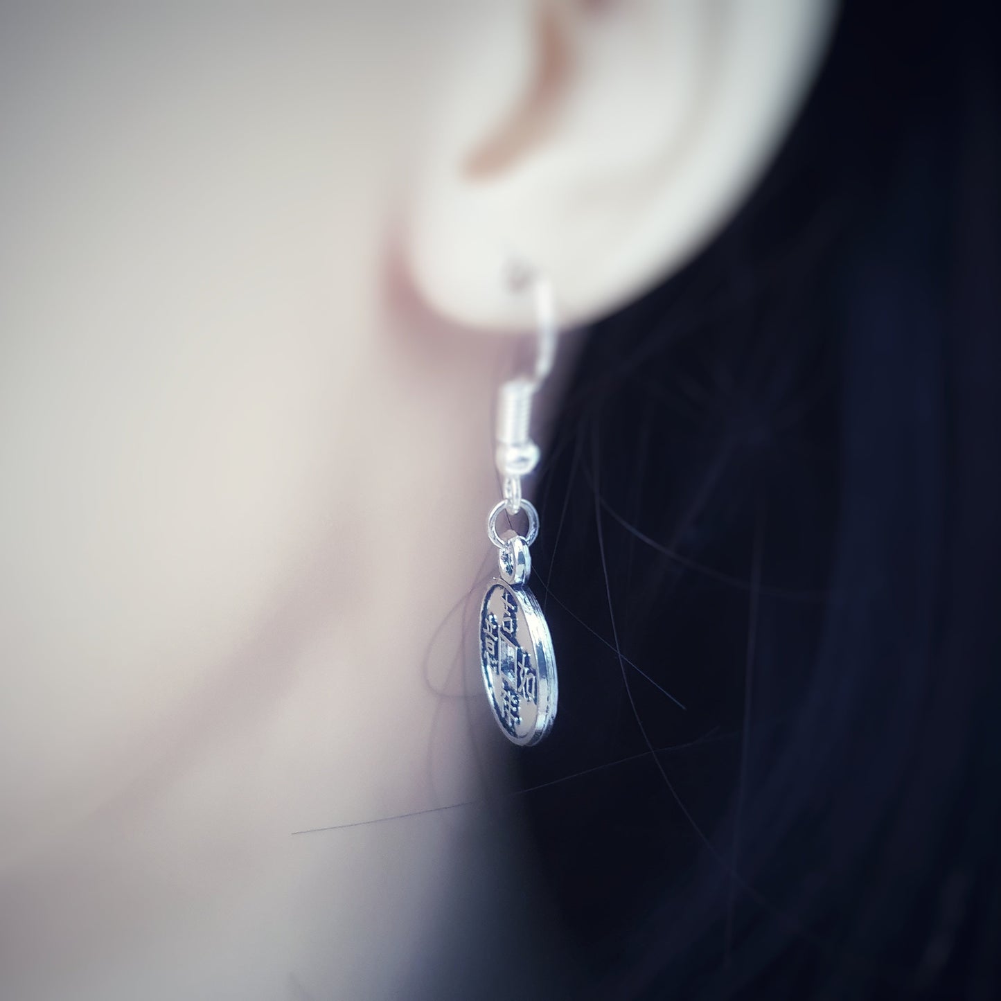 Close-up of a silver earring worn on an ear with a blurred background