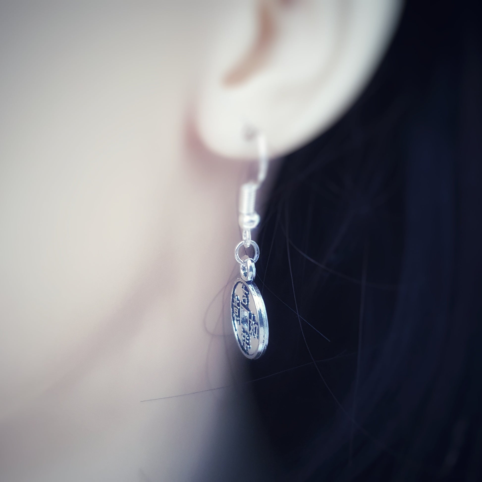 Close-up of a silver earring worn on an ear with a blurred background