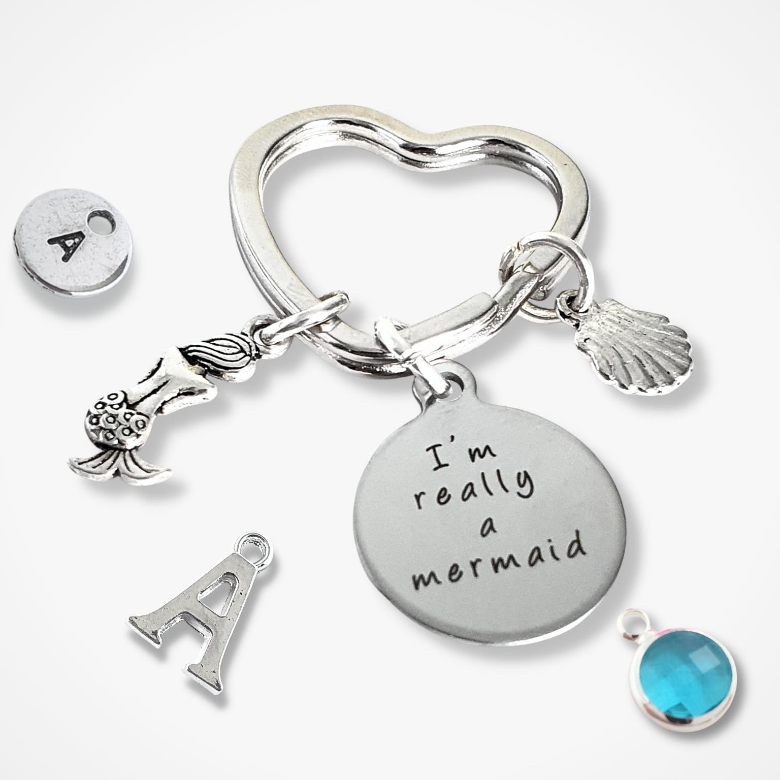 Silver keychain with charms including a mermaid, letter 'A', shell, and blue birthstone on a white background.