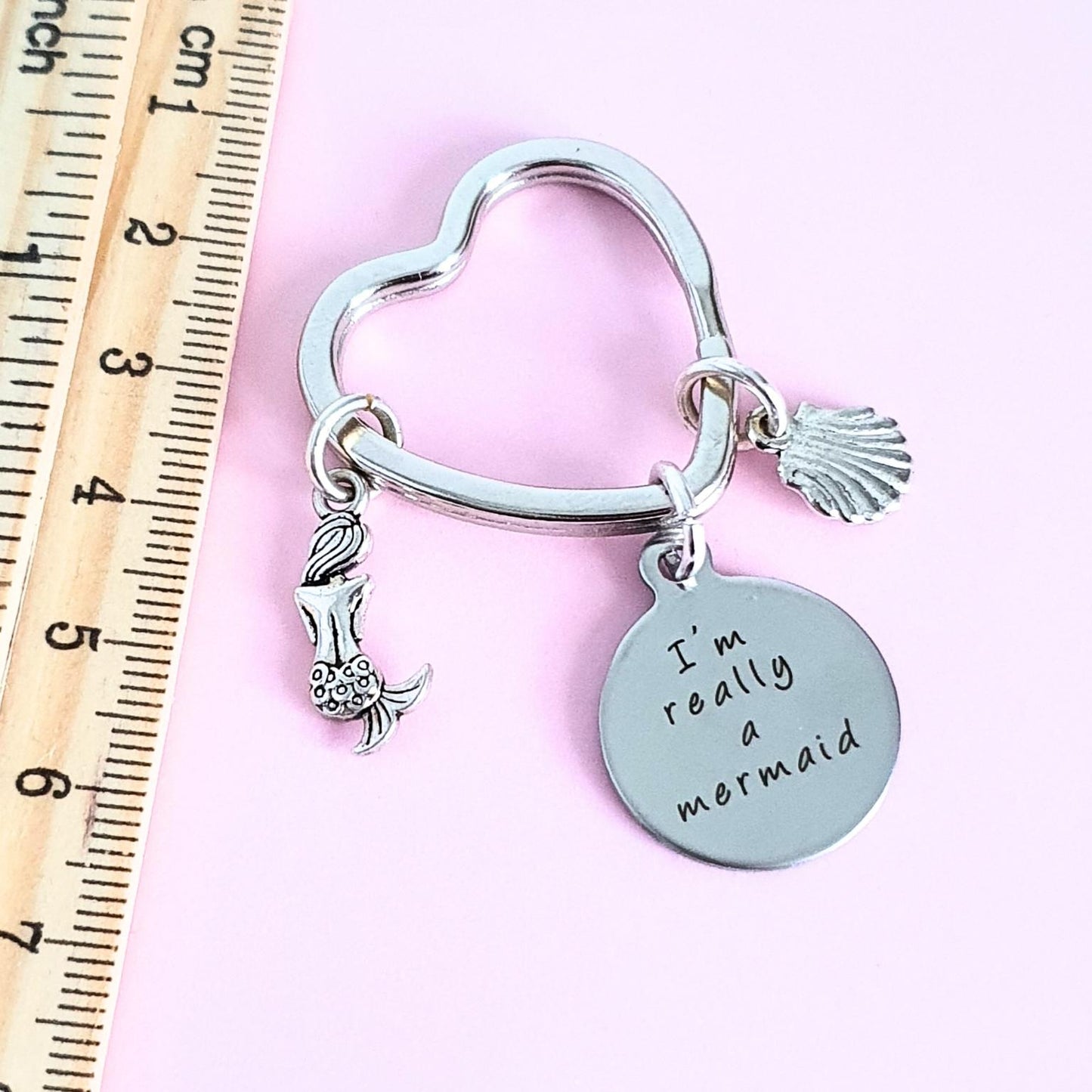 Keychain with mermaid charm and 'I'm really a mermaid' tag next to a ruler on a pink background