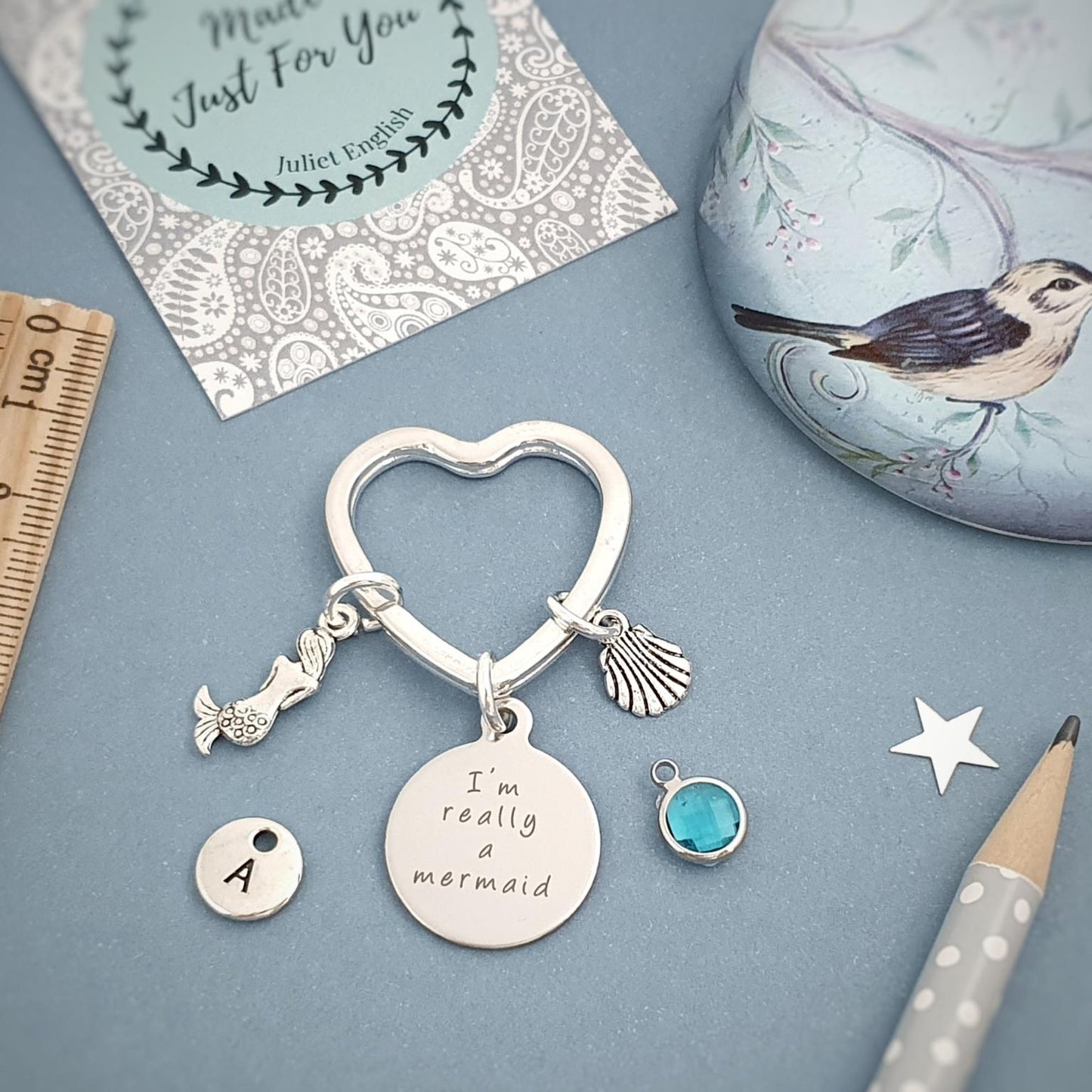 Silver heart-shaped keychain with charms on a blue surface with a ruler and decorative card.