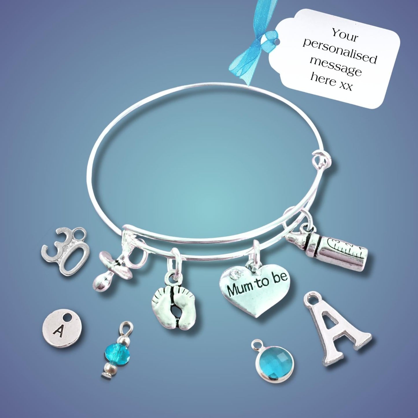 A silver bangle bracelet with multiple charms, including a heart charm that says 'Mum to be', a footprint charm, and letter charms, displayed on a blue gradient background with a white customization tag.