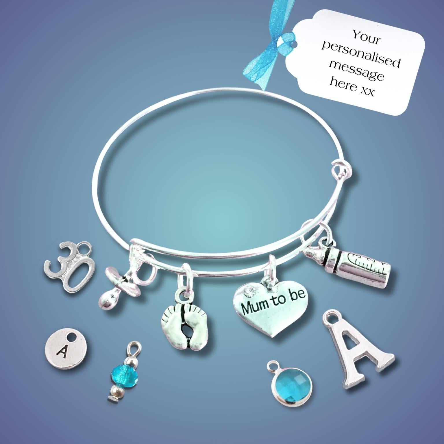 A silver bangle bracelet with multiple charms, including a heart charm that says 'Mum to be', a footprint charm, and letter charms, displayed on a blue gradient background with a white customization tag.