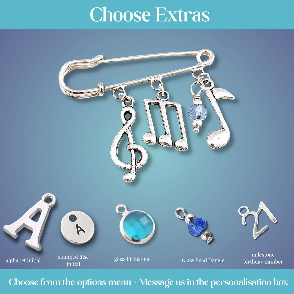 Silver safety pin brooch with music note charms and customizable letter or gemstone options, shown on a blue gradient background with text reading 'Choose Extras'.