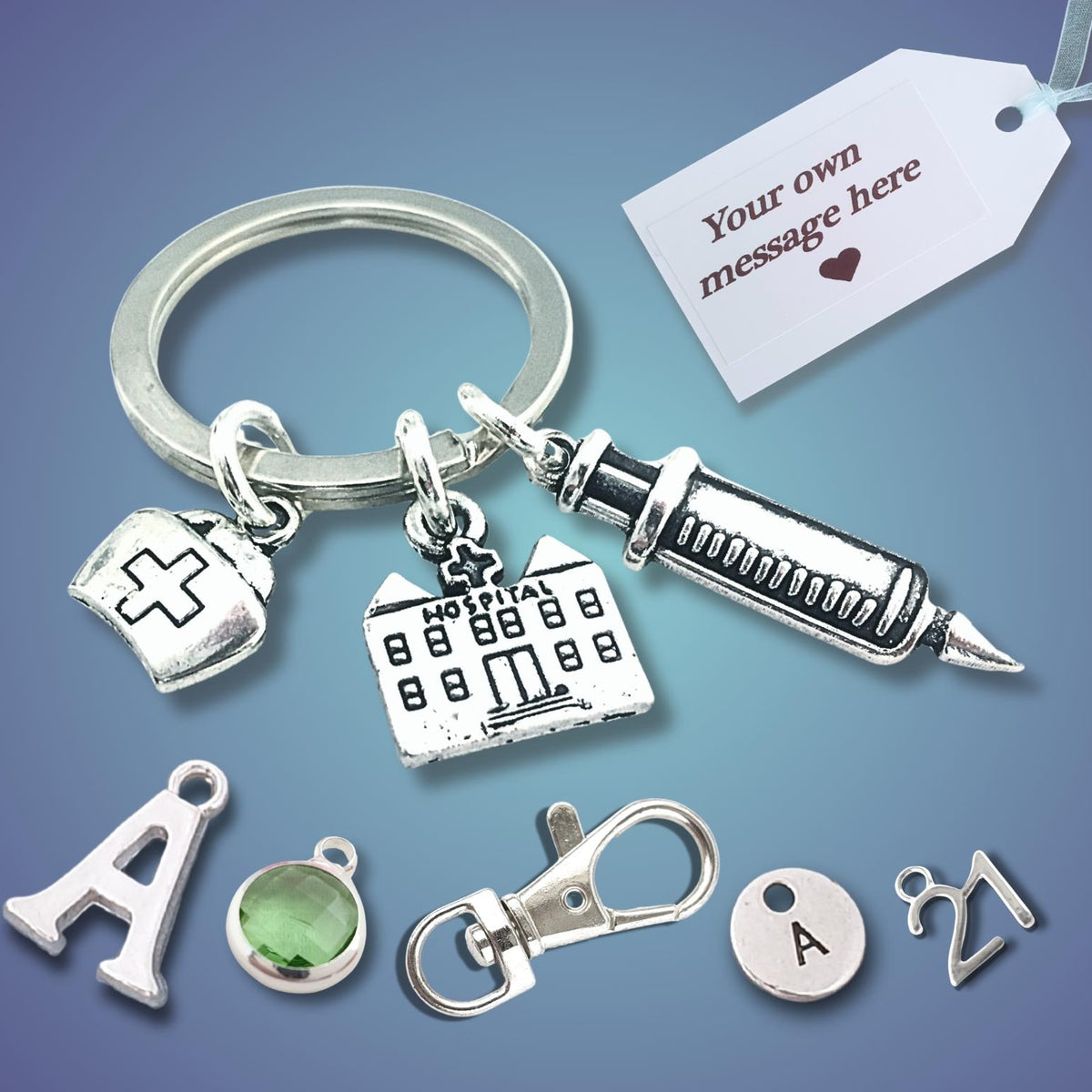 Silver-tone keychain with medical-themed charms including a syringe, hospital building, and nurse hat, shown with a customizable message tag and letter initial charms on a blue gradient background.