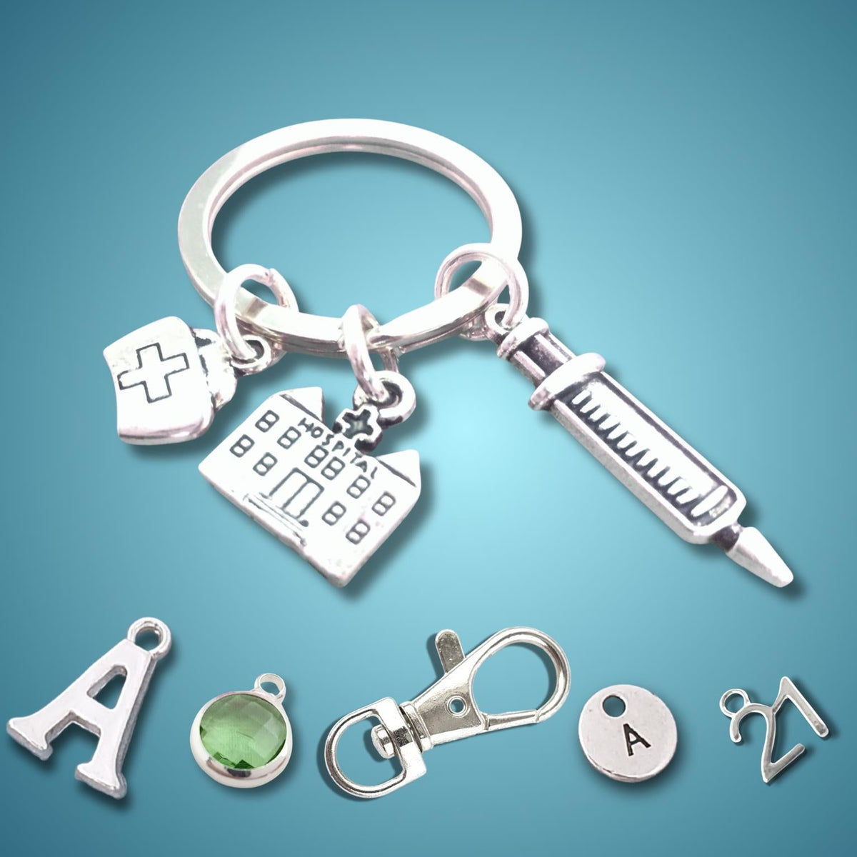A silver keychain with medical-themed charms, including a syringe, a hospital and a nurse hat, displayed on a blue gradient background with additional loose charms below.