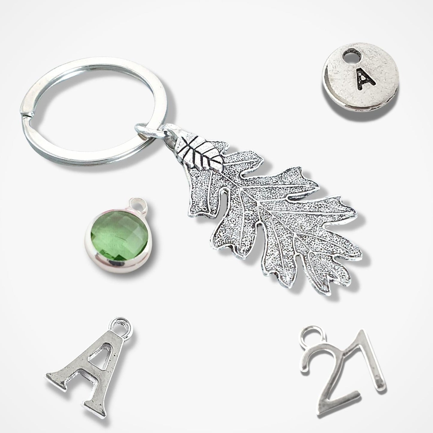 Silver keychain with leaf charm, green gemstone, and letter 'A' tag on a white background