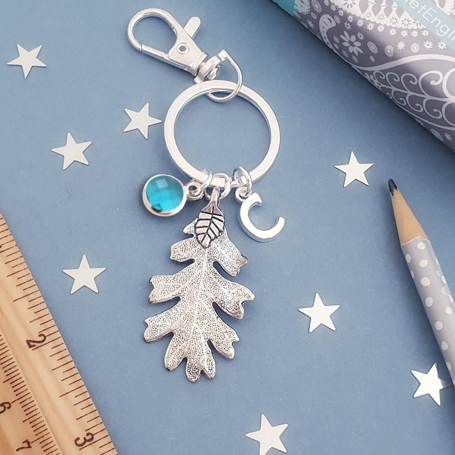 Silver keychain with leaf charm on a blue surface with stars and a ruler.