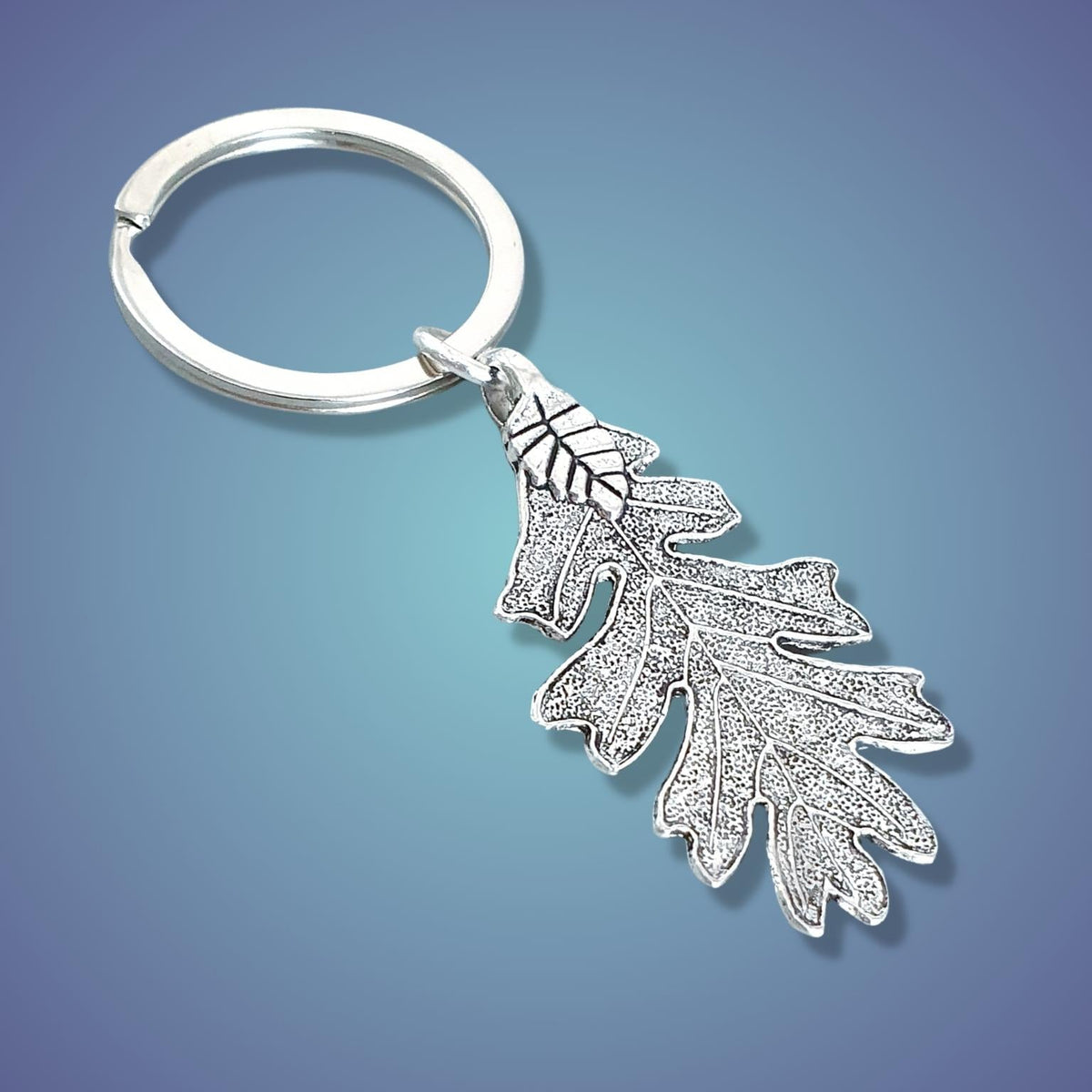 A silver metal keychain featuring a detailed leaf pendant, shown on a blue gradient background.