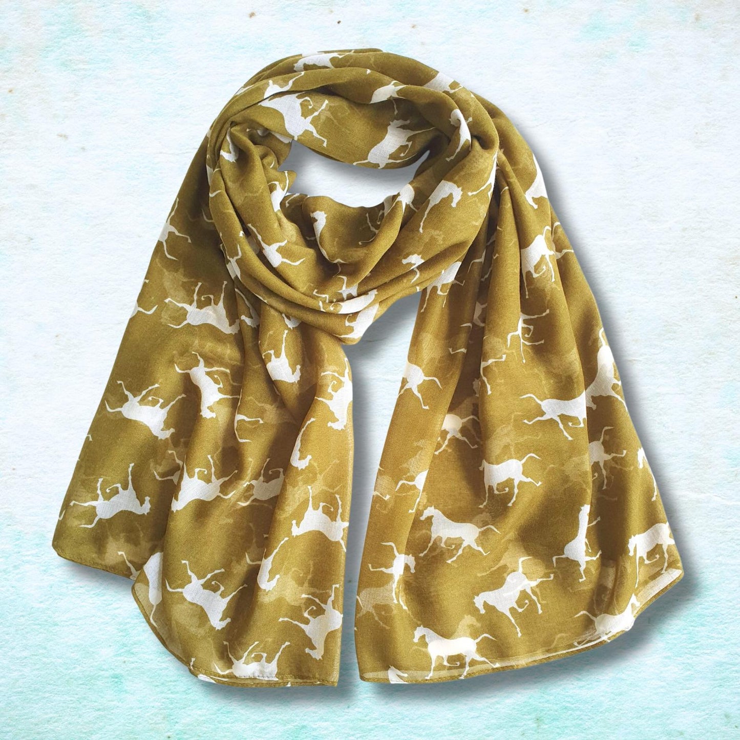 A green yellow scarf with a white repeating pattern of horse silhouettes, styled in a loose loop on a textured light blue background.