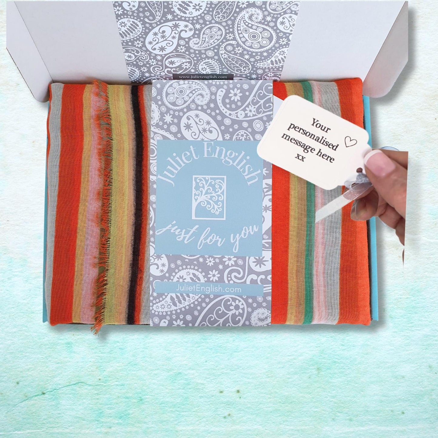 Striped scarf with a personalized tag in a gift box, featuring the brand 'Juliet English'.