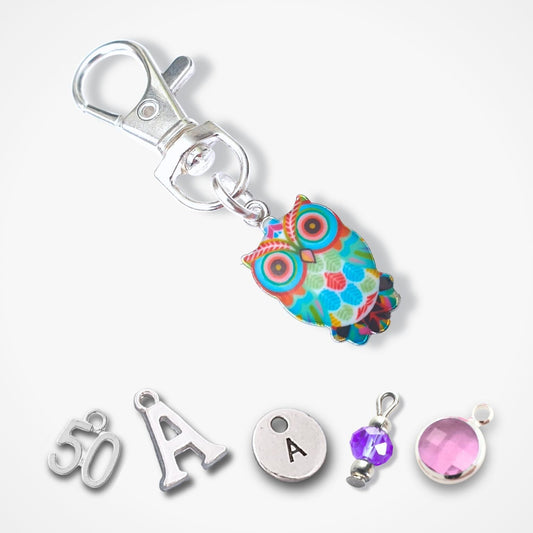 A silver-toned keychain clasp with a colorful owl charm in shades of blue, green, orange, and pink, displayed above five small silver jewelry components on a light gray background.