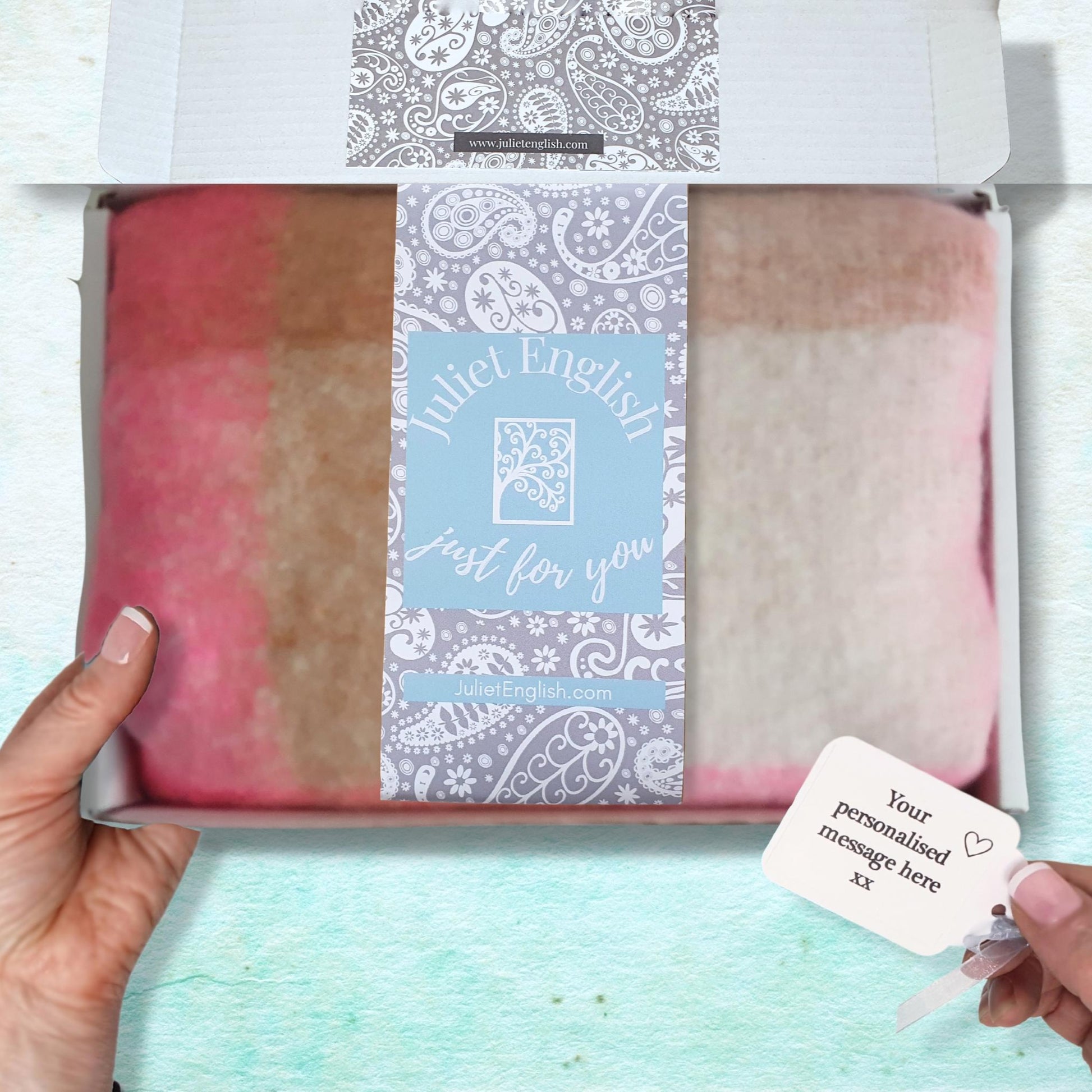 Packaged product with a personalized message tag held by hands against a light blue background