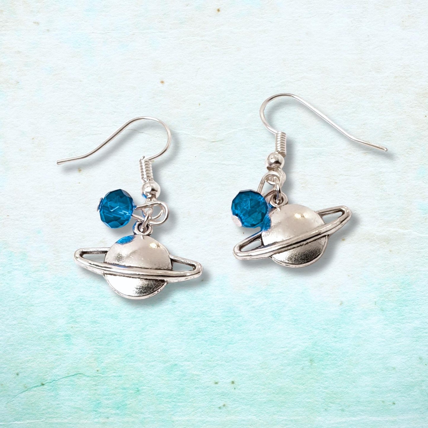 Planet-themed earrings with blue beads on a light blue background