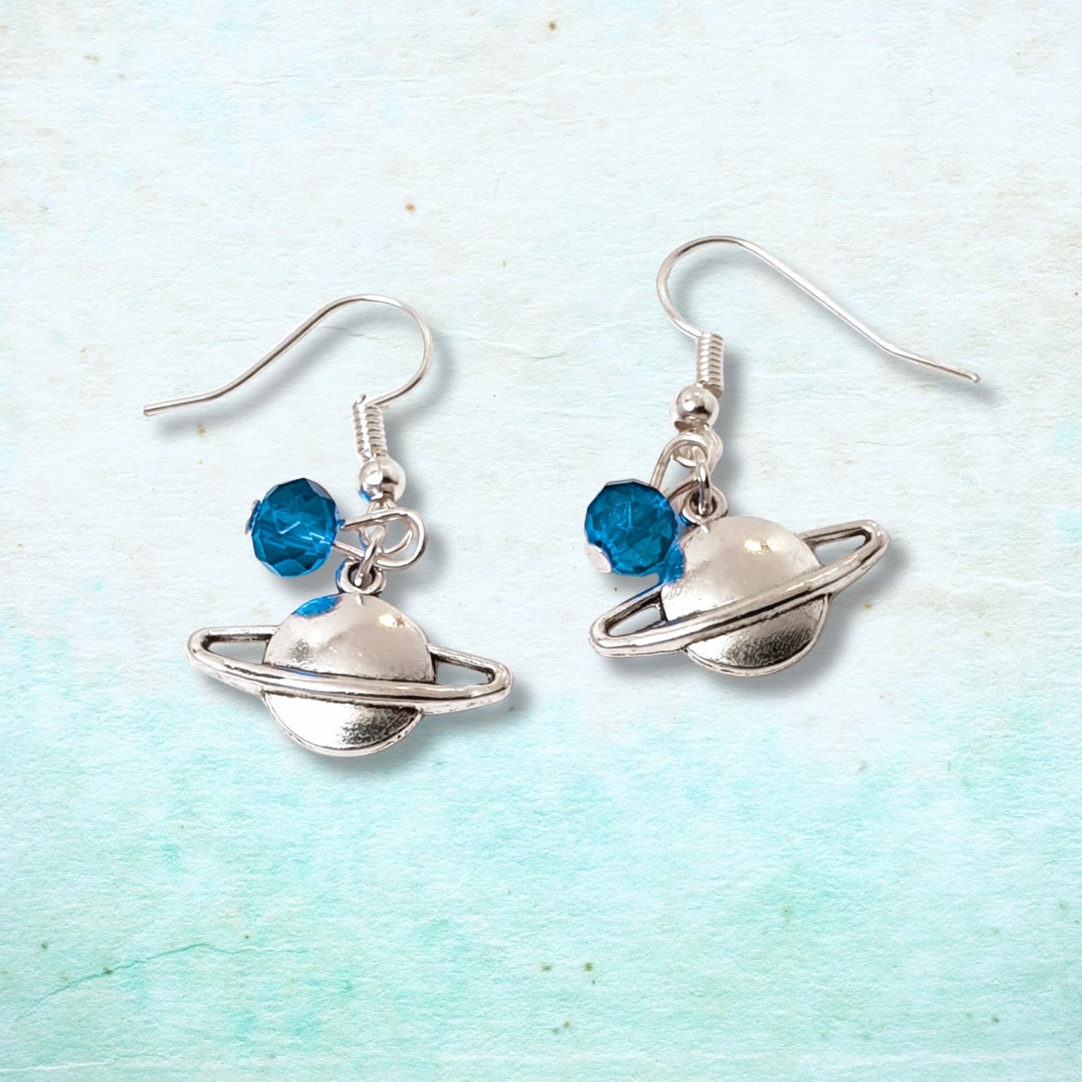 Planet-themed earrings with blue beads on a light blue background
