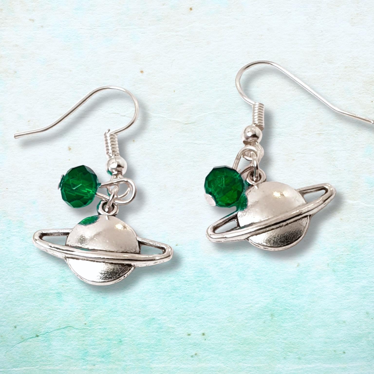 Silver planet-shaped earrings with green beads on a light blue background