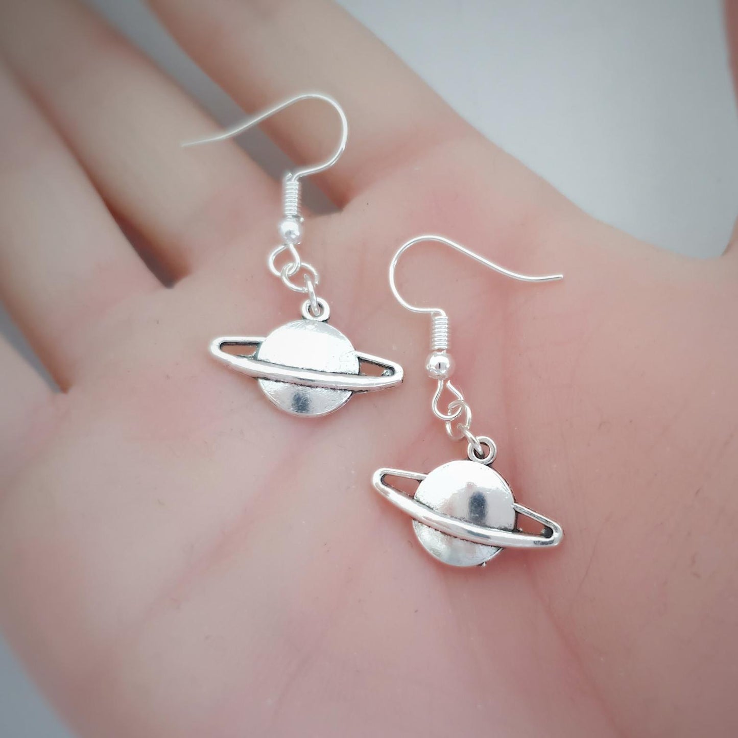 Silver planet-shaped earrings on a hand