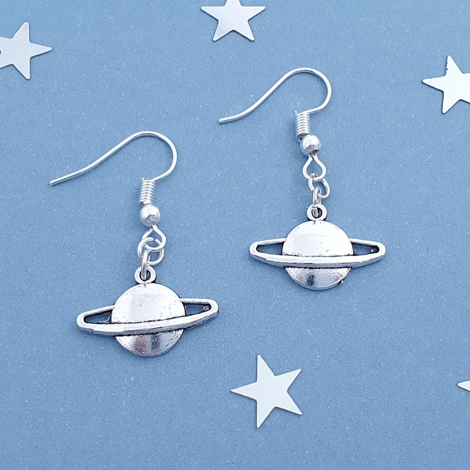 Silver planet-shaped earrings on a blue background with star decorations