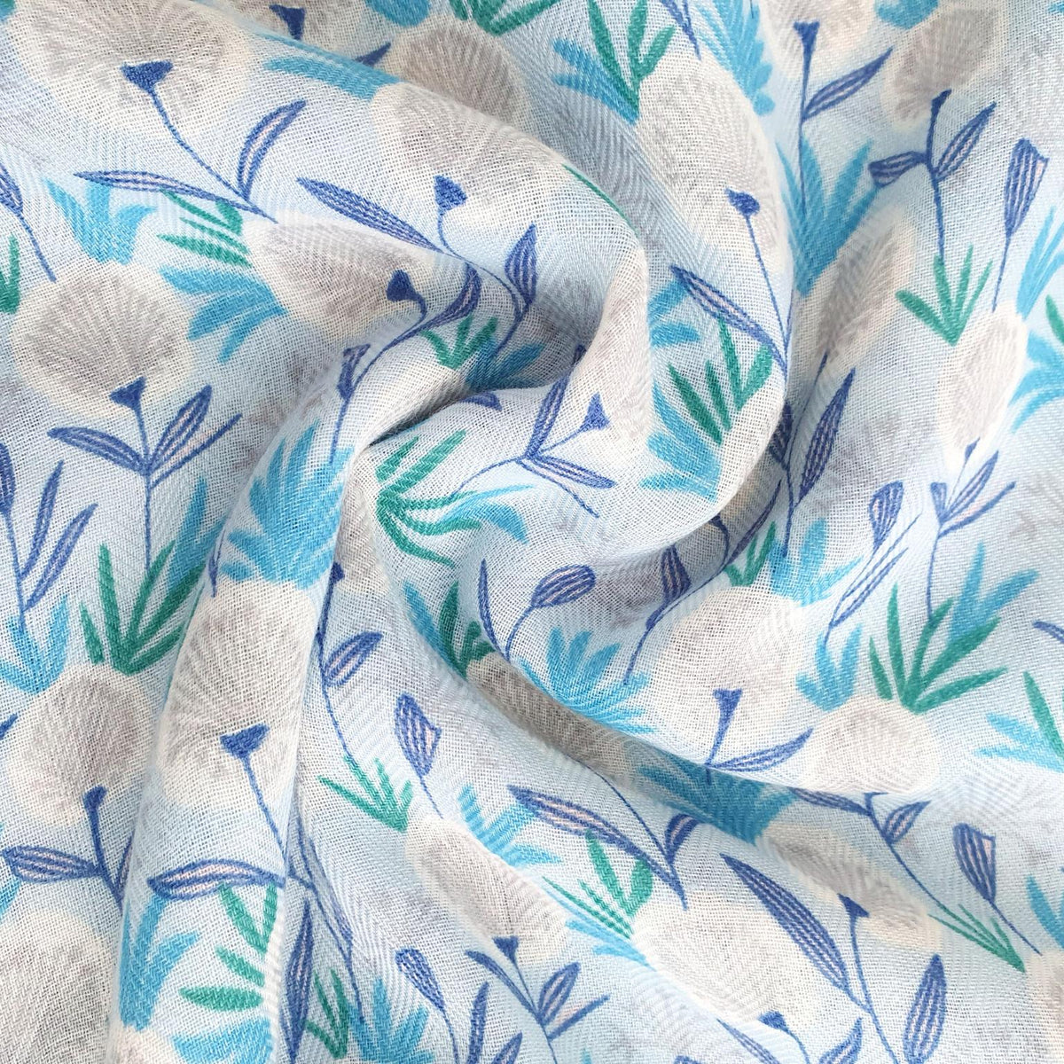 A close-up of a draped fabric with a textured, woven pattern featuring cream-colored flowers, blue stems, and green leaves on a white background.