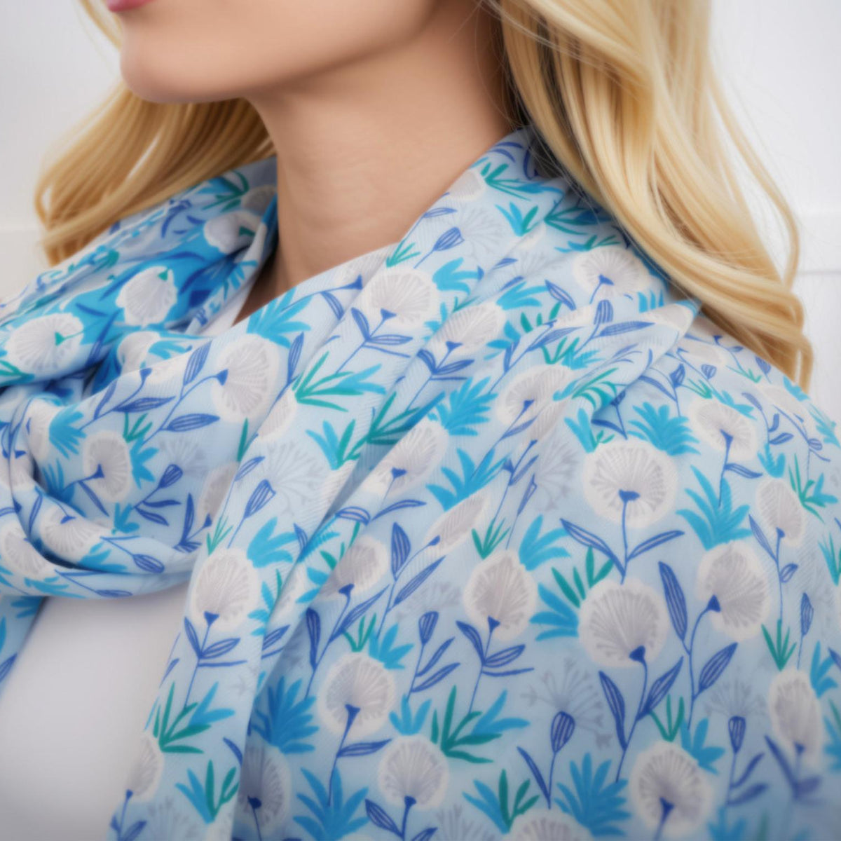A close-up of a blonde woman wearing a light blue scarf with a white and blue floral pattern.