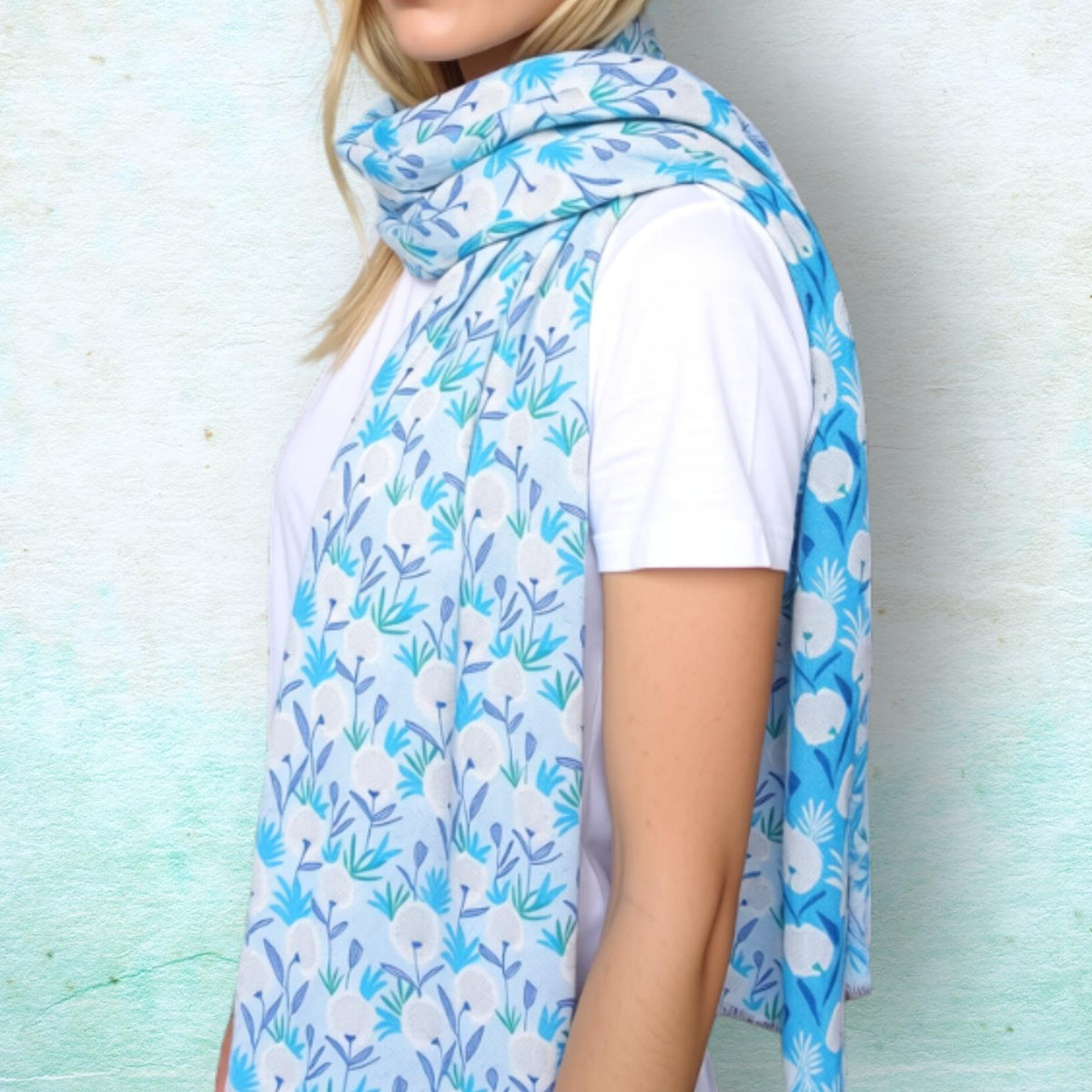 A woman wearing a white t-shirt and a light blue and white floral print scarf, standing against a textured light blue wall.