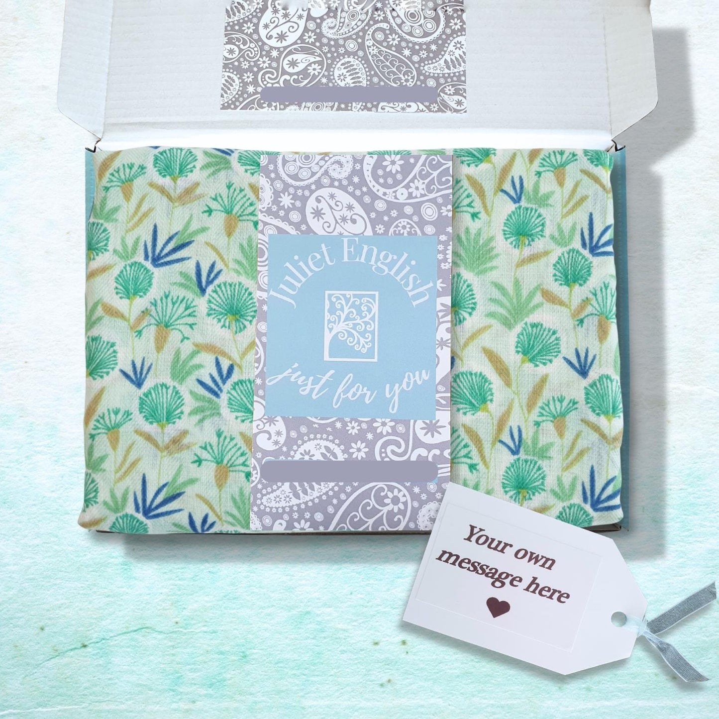 A gift box with scarf featuring green and blue botanical patterns on a light background, with a central light blue panel reading 'Juliet English Just for you' and a small white gift tag attached.