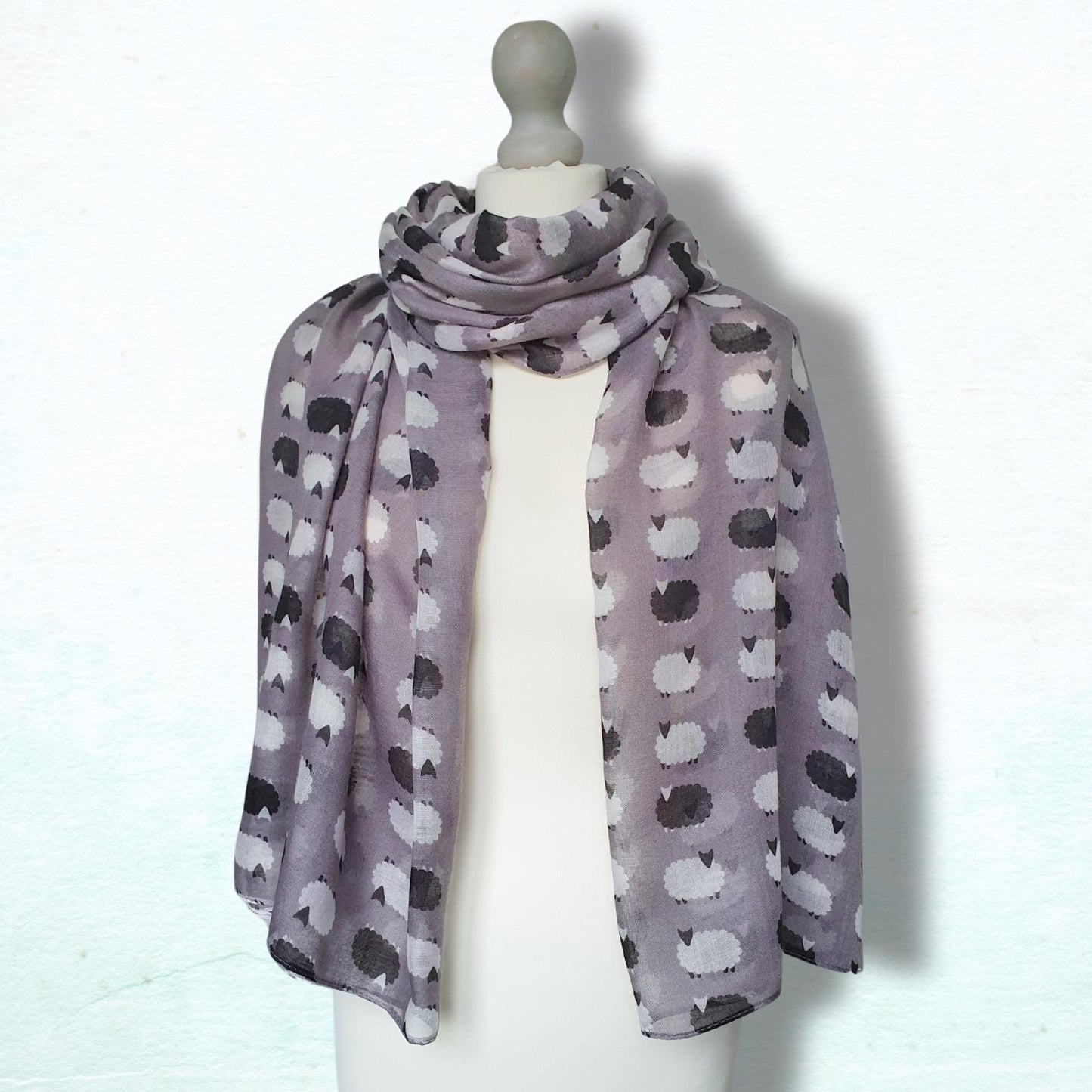 Scarf with a sheep pattern draped over a mannequin on a white background