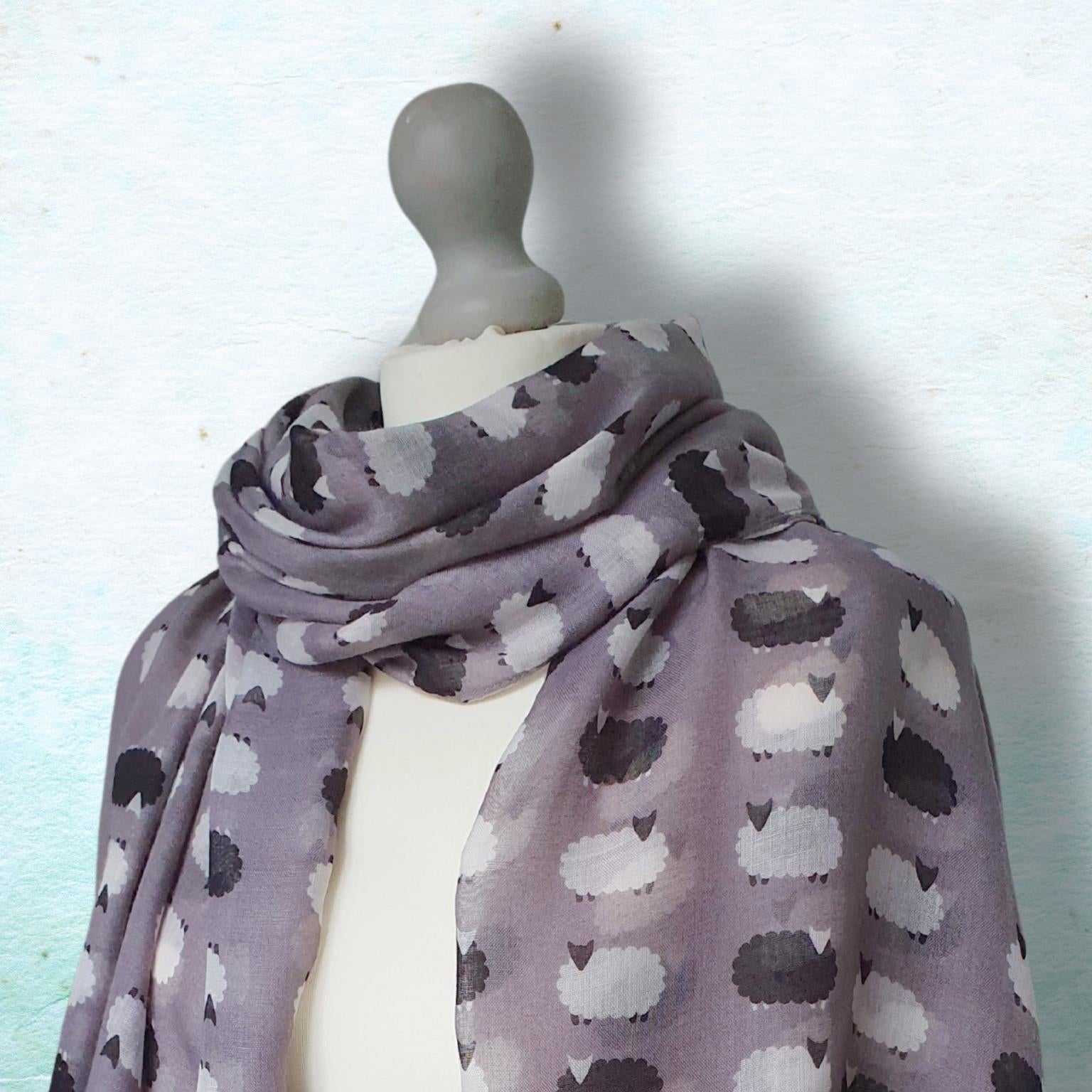 Mannequin wearing a grey scarf with sheep pattern against a light blue background