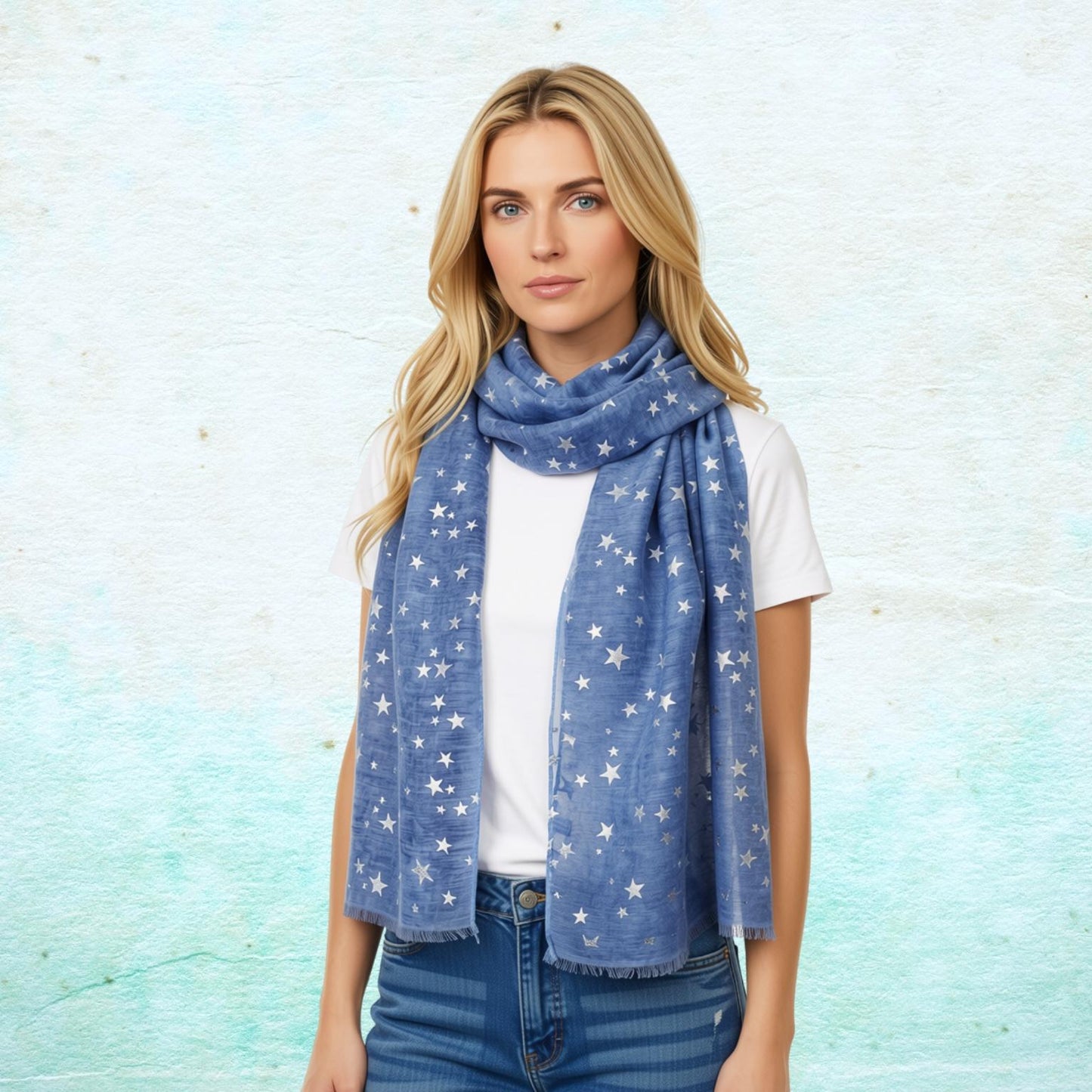 A blonde woman wearing a blue scarf with a silver star pattern, styled over a white t-shirt and blue jeans, standing against a textured light blue background.