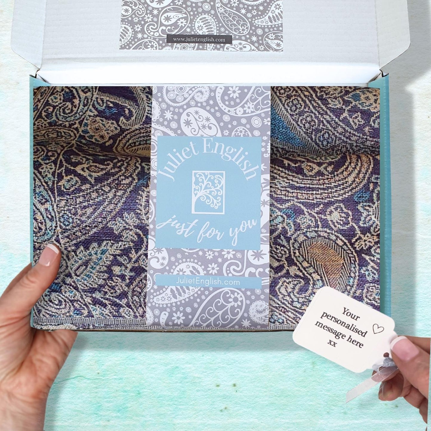Packaged scarf with paisley patterns and a personalized message card on a light blue background