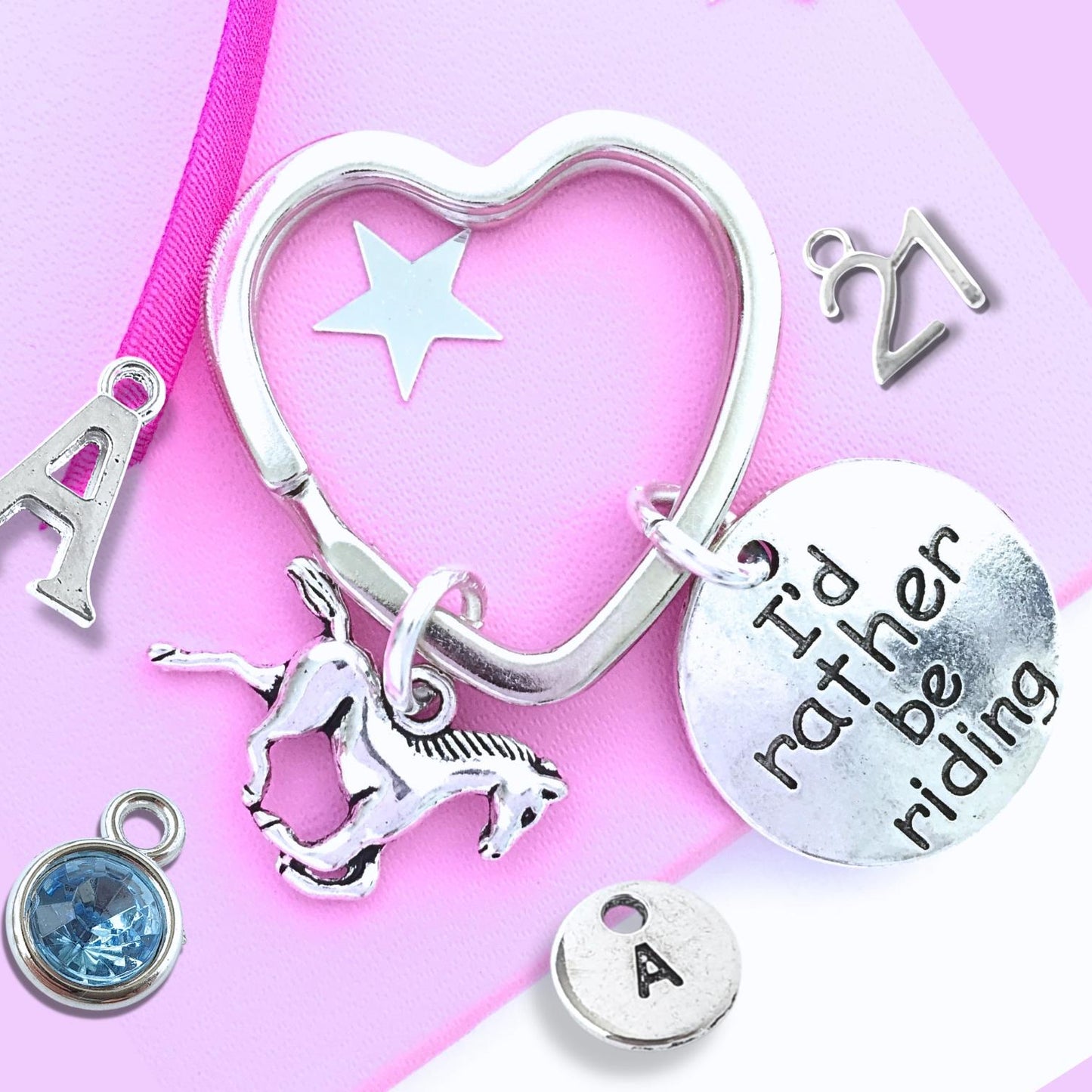 Silver heart-shaped keychain with various charms on a pink background