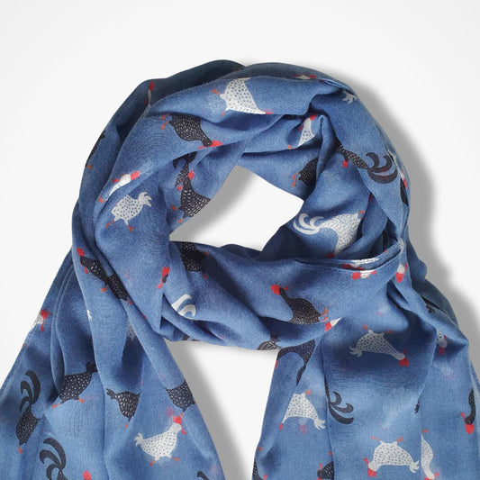 A blue scarf with a pattern of stylized chickens in black, white, and red, draped against a light gray background.